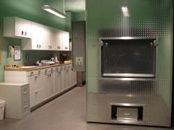 A laboratory or morgue setting featuring white cabinets, a light green wall, and a large metal cremation unit.