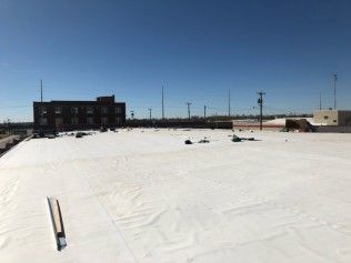 A bright, expansive flat white roof on a commercial building under a clear blue sky.