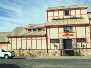 A large, multi-level building with beige stucco, orange trim, and a metal roof, with a white truck parked in front.