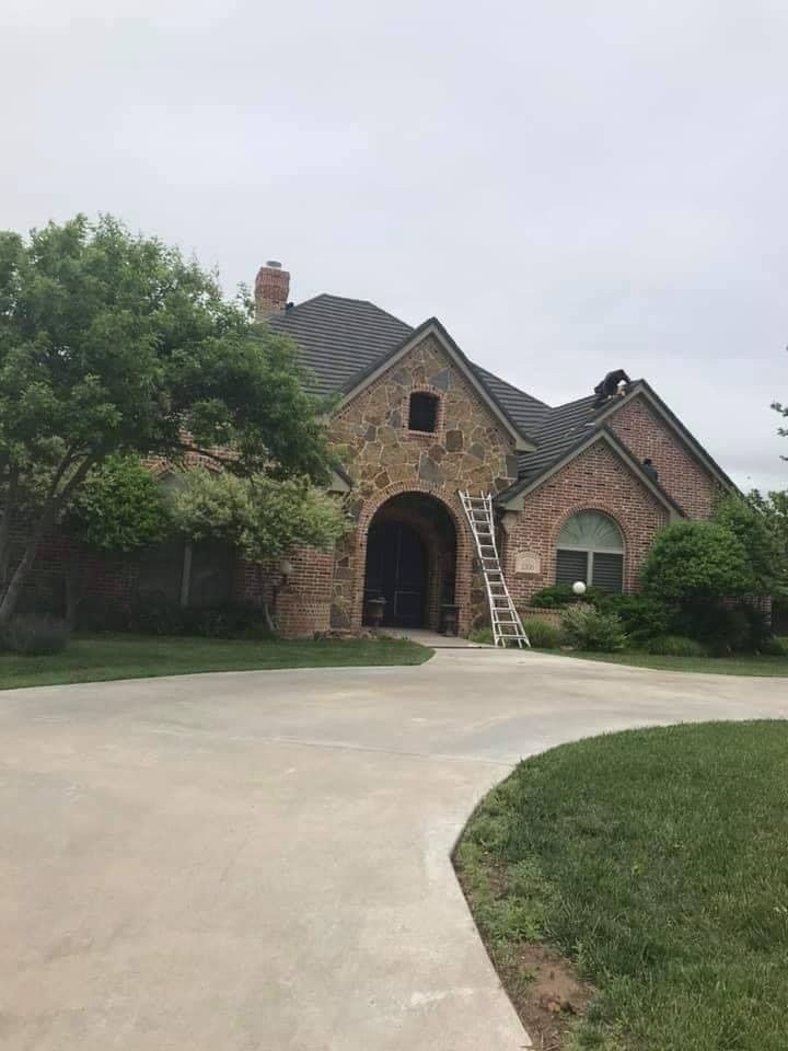A large, two-story stone and brick house with a dark gabled roof and a ladder leaned against the front entrance.