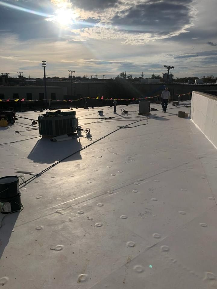 A person walks across a white, flat commercial roof featuring a mechanical unit under a bright, sunny sky.