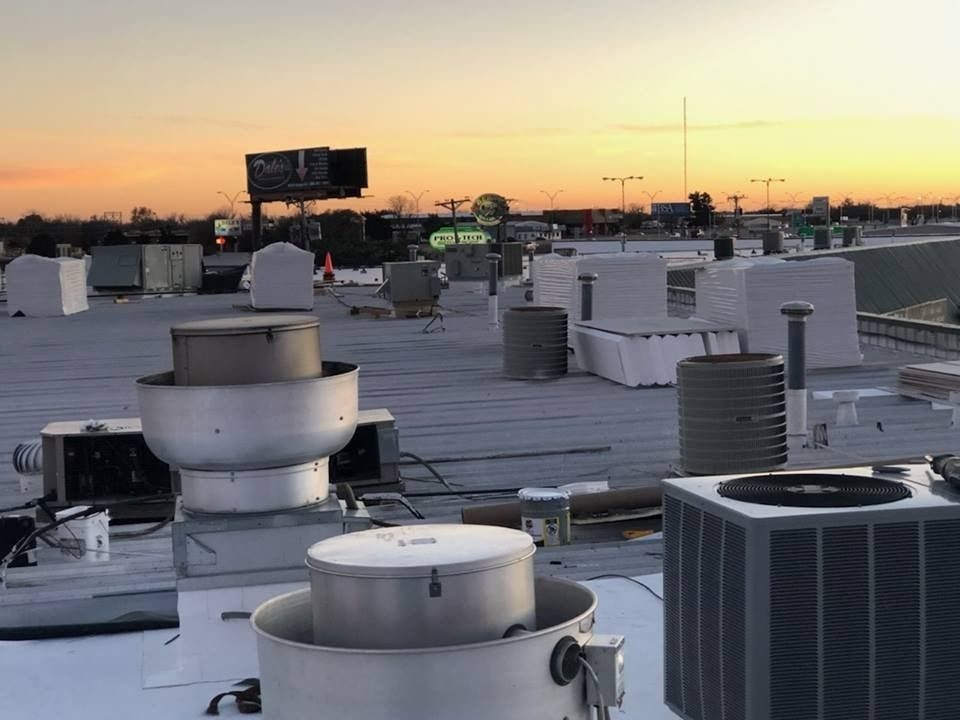 A sunset view of a flat commercial roof featuring multiple HVAC exhaust fans, vents, and units.