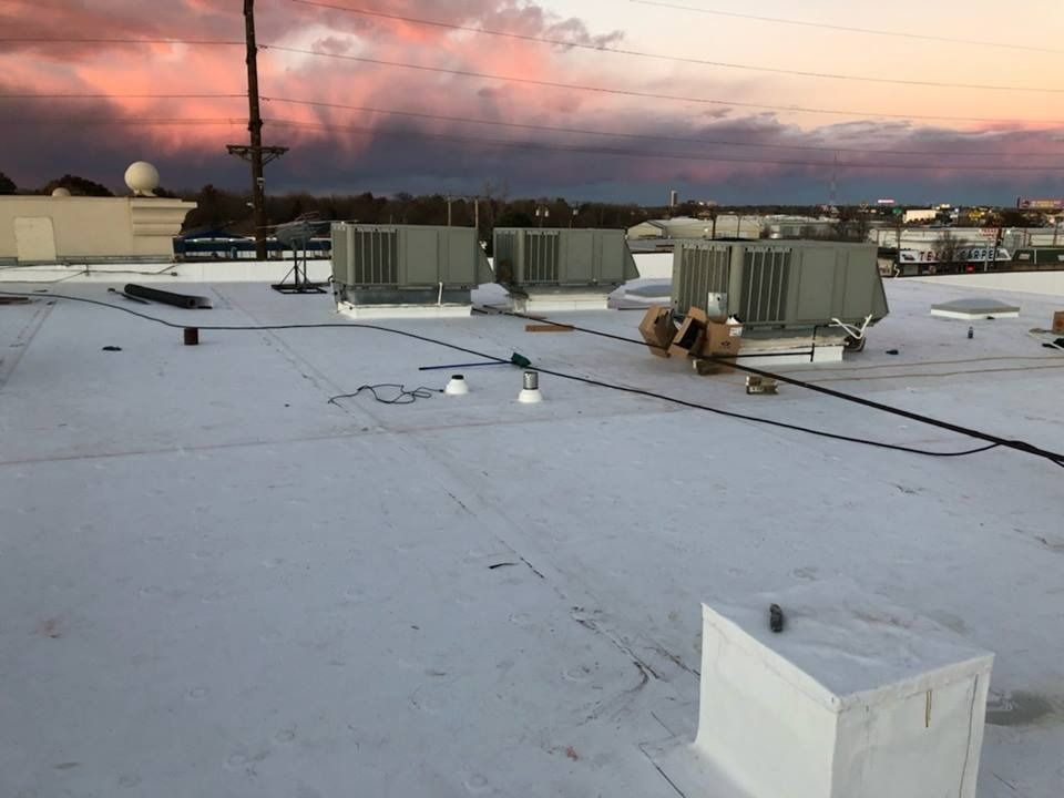 A flat rooftop with three HVAC units, a small boxy structure, and scattered wiring against a colorful sunset sky.