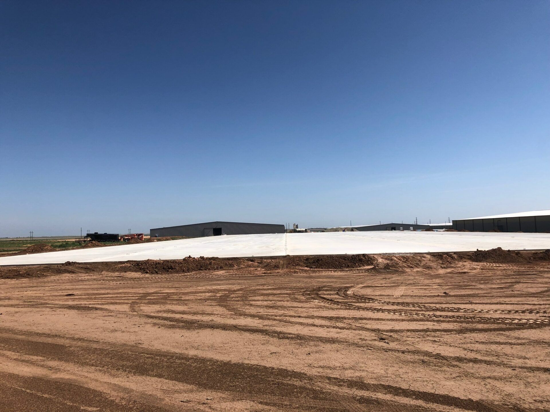 A large, newly poured concrete slab at a construction site with dirt in the foreground under a clear blue sky.