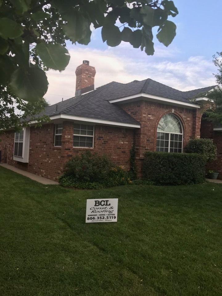 A red brick house with a dark roof and an arched window stands behind a green lawn with a BCL construction sign.