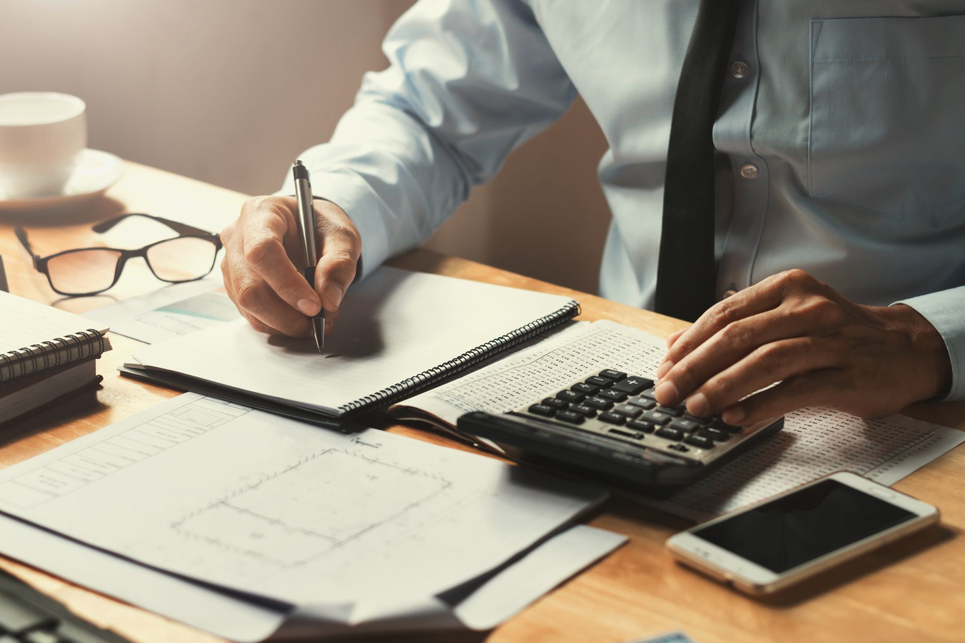 Man in business attire calculating with calculator, writing on notepad at desk.