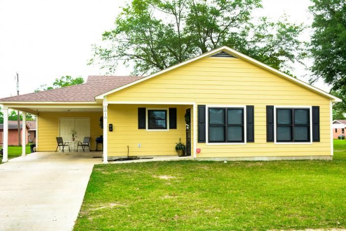 Yellow single-story house with black shutters, front lawn, and covered carport