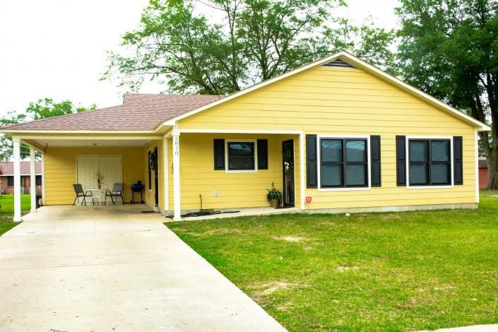 Yellow single-story house with attached carport, concrete driveway, and green lawn