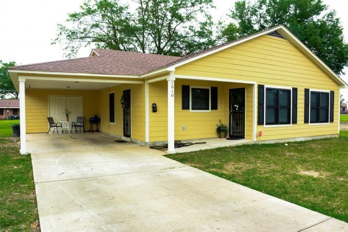 Yellow house with a carport, black shutters, and a concrete driveway in a grassy yard
