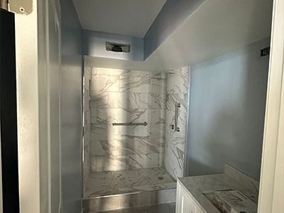 A walk-in shower with white and grey marble-patterned tile, featuring horizontal and vertical silver grab bars.