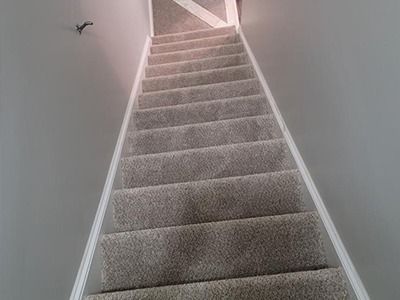 A carpeted staircase with grey walls and white trim, viewed from the bottom looking up toward the landing.