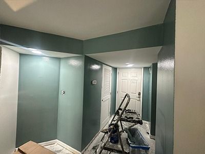 A room under renovation with teal painted walls, a white louvered door, a closed white door, and a metal step ladder.
