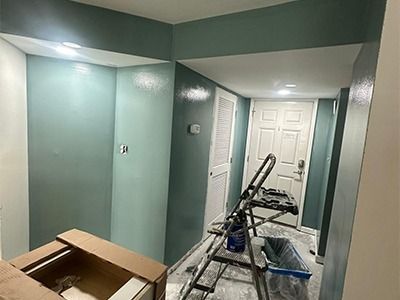 A hallway with teal-painted walls, a closed white door, a folding ladder, and a box being prepared for a renovation project.