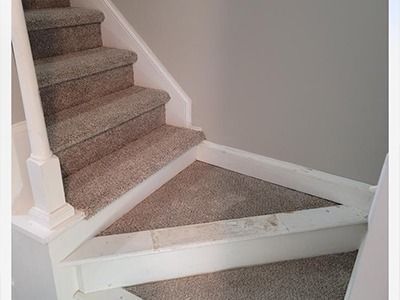 A staircase with grey carpeted steps, white wooden trim, and a white baluster against a light grey wall.