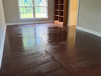 A dark, glossy hardwood floor in a room with light grey walls, a window with blue tape, and a wooden bookshelf.