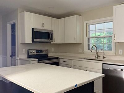 A modern kitchen with white cabinets, light countertops, a stainless steel oven and microwave, and a window above the sink.