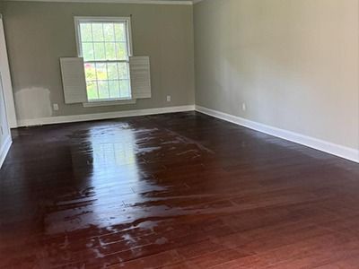 An empty room with light gray walls, dark wood floors, white trim, and a window with white shutters.