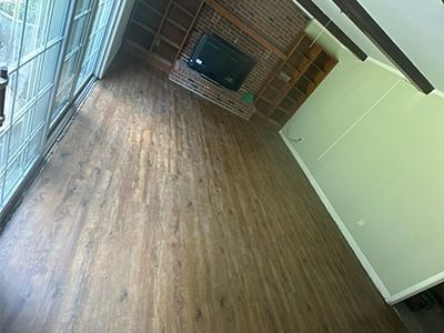 A wide-angle view of an empty room with wood-look flooring, a brick fireplace, and built-in shelving, next to sliding doors.