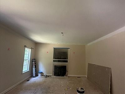 An interior view of a room under renovation with beige walls, a fireplace in the center, and bare floors.