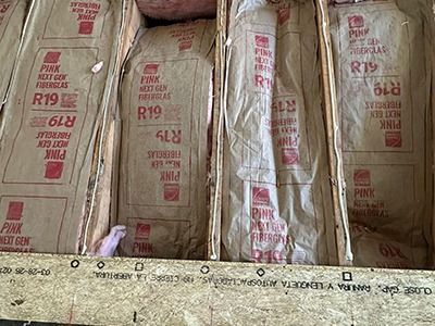R19 pink fiberglass insulation batts installed between wooden floor joists in an unfinished subfloor.