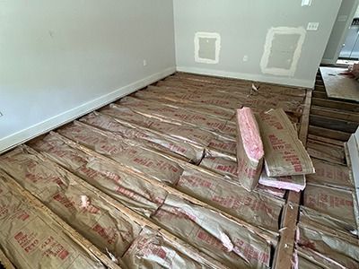 Floor joists in an unfinished room, with pink fiberglass insulation batts placed between them.