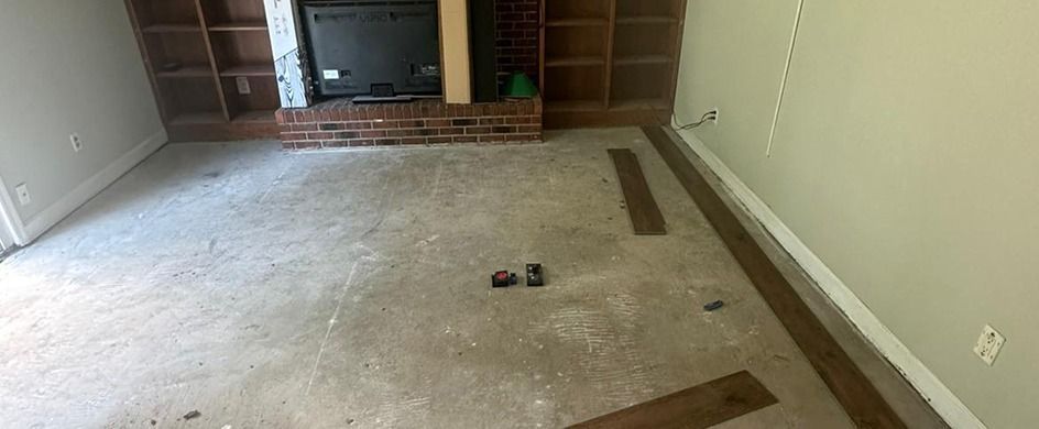 An interior room with a fireplace and wood shelving undergoing a floor renovation, showing some new dark planks installed.