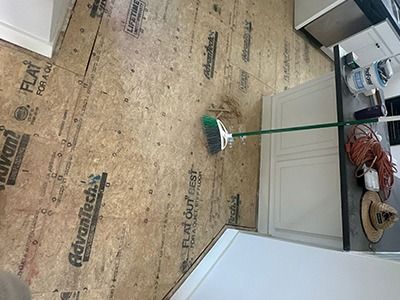 A broom sits on an Advantech subfloor near white kitchen cabinets and a counter with construction gear.