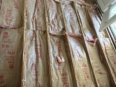 R-19 fiberglass insulation batts with paper facing installed between wooden wall studs.