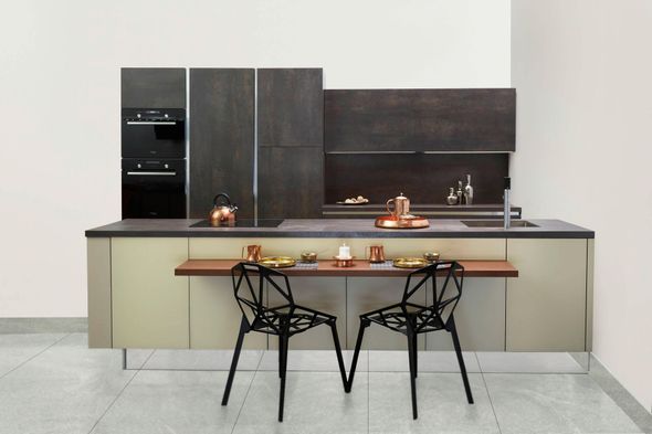 A modern kitchen with dark wood cabinets, light cream island, and two black geometric chairs at a breakfast bar.