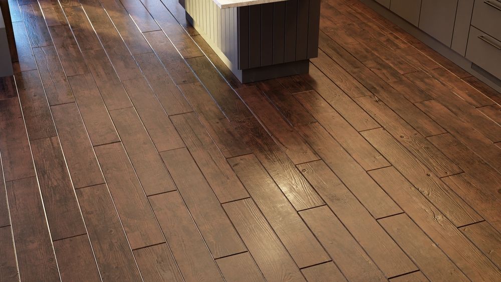 A high-angle view of a kitchen floor with dark brown wood-plank flooring featuring visible horizontal nail patterns.