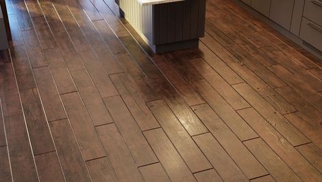 A high-angle view of a kitchen floor with dark brown wood-plank flooring featuring visible horizontal nail patterns.
