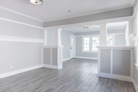 An empty room with light gray walls, white trim, and light wood floors, divided by two half-walls with pillars.