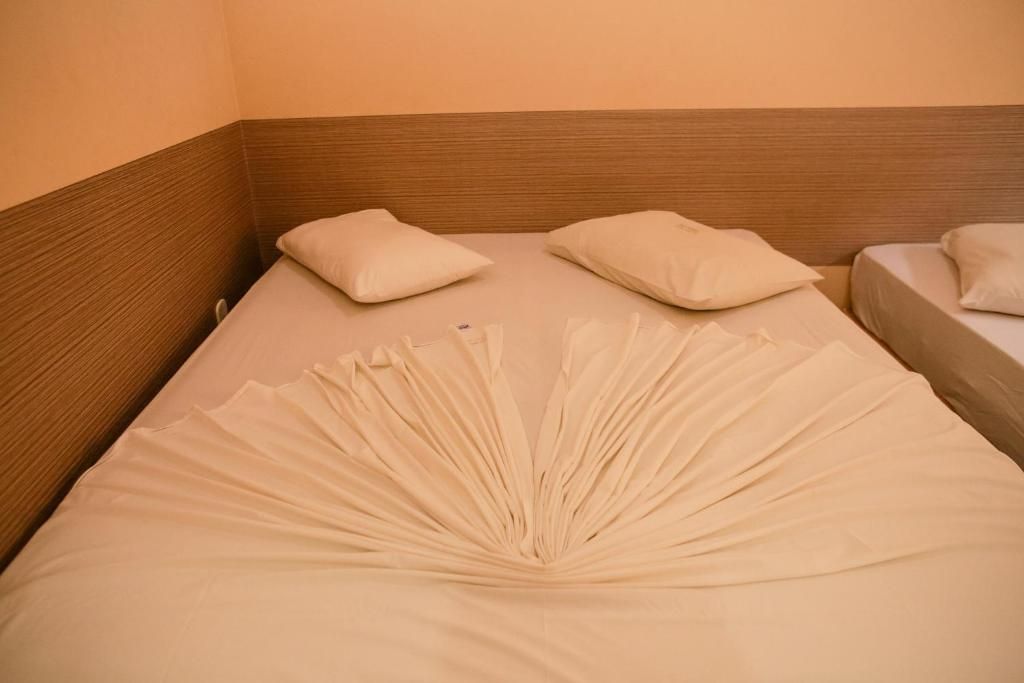 Uma cama de hotel com lençóis brancos, dois travesseiros e um tecido decorativo dobrado em leque ao centro do colchão.
