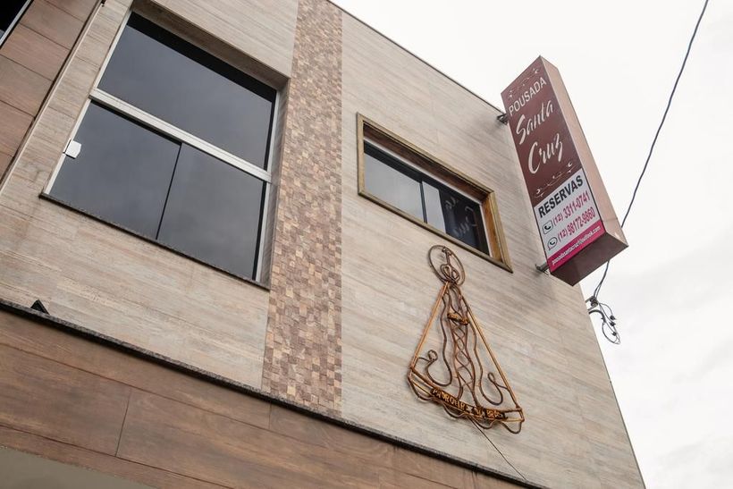 Um prédio bege de vários andares com uma placa vertical, janelas escuras e o contorno de uma figura religiosa desenhado com arame na parede.