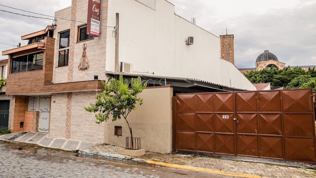Um edifício de dois andares com paredes de pedra bege e brancas, um portão de metal marrom e uma estrutura em forma de cúpula visível ao fundo.