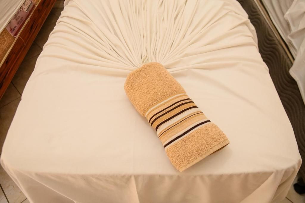 Uma maca de massagem com um lençol branco aberto em uma das extremidades e uma toalha bege estampada dobrada no centro.