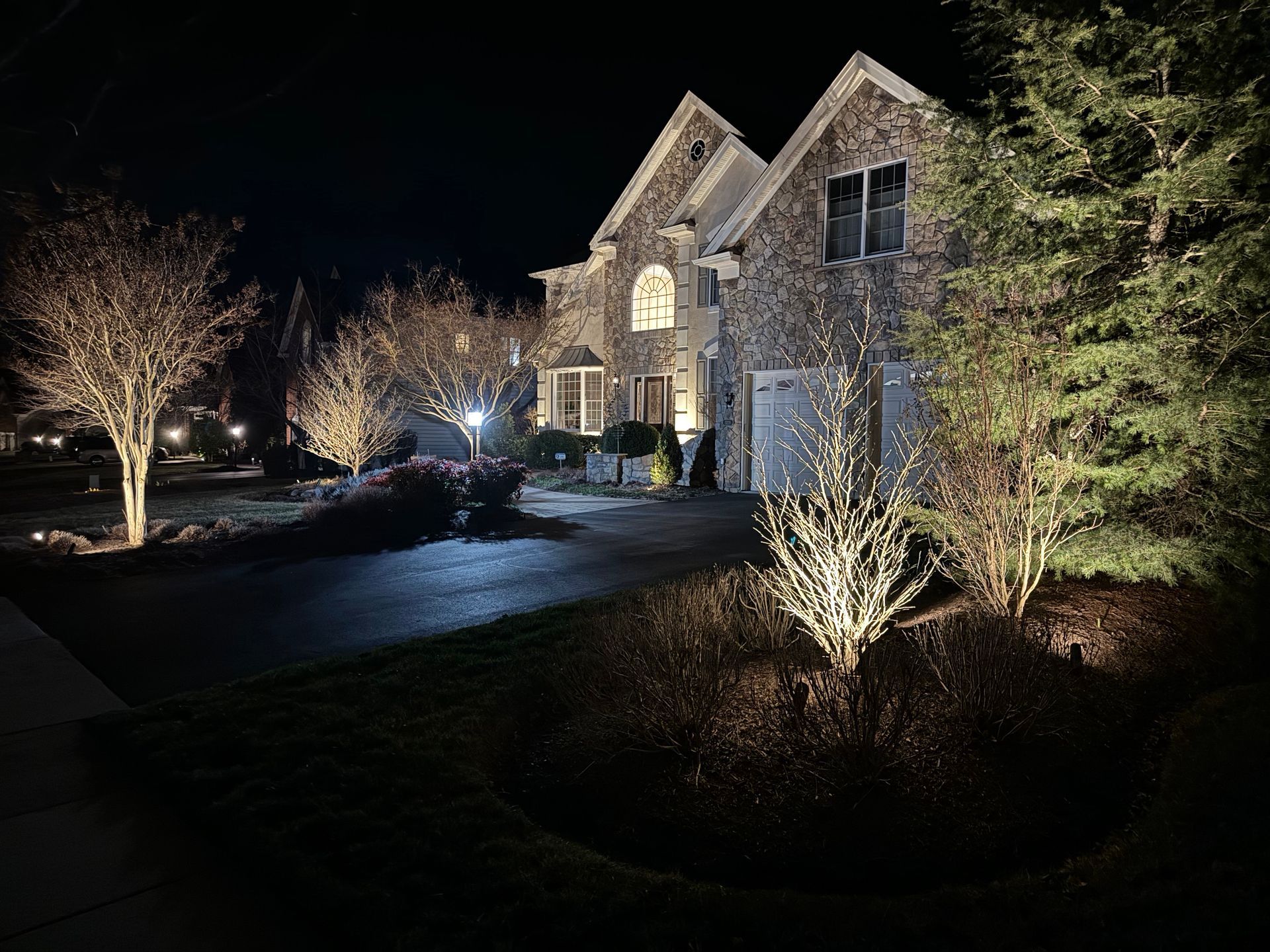 A large house is lit up at night with trees in front of it.