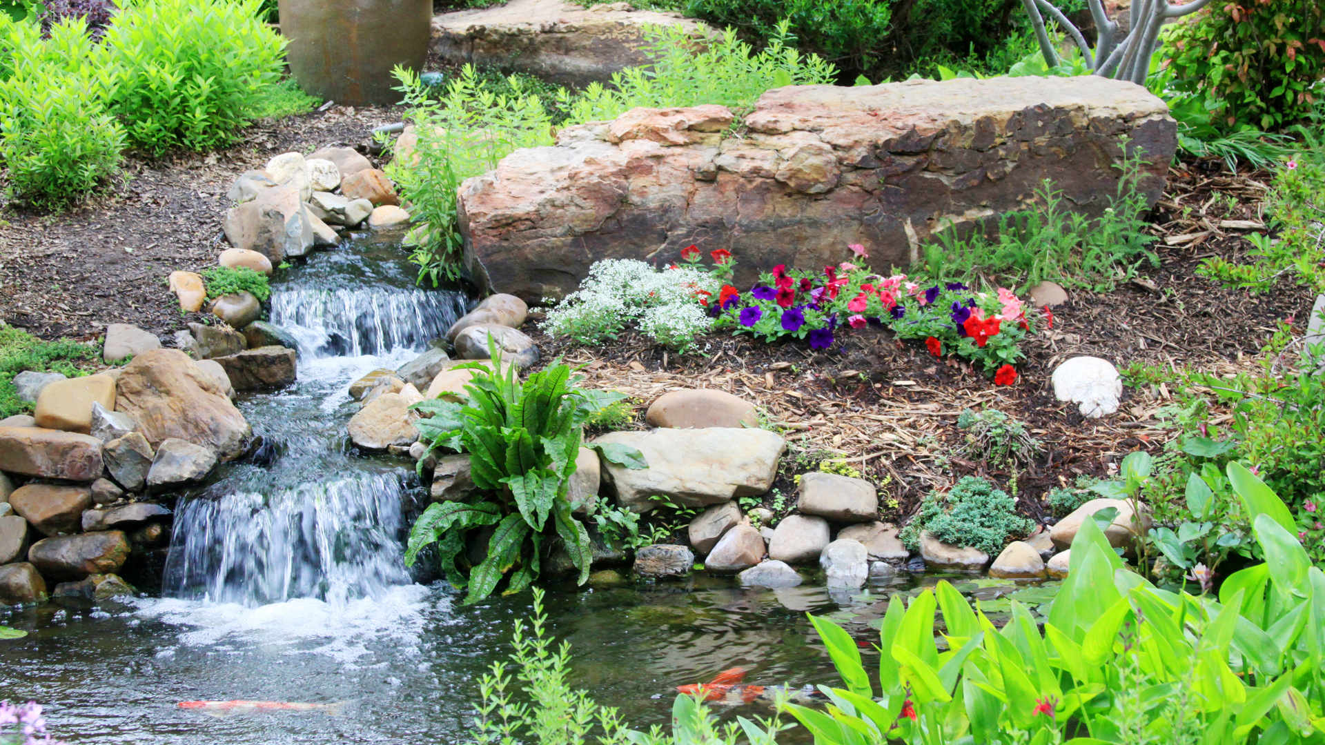 A waterfall is surrounded by rocks and flowers in a garden.