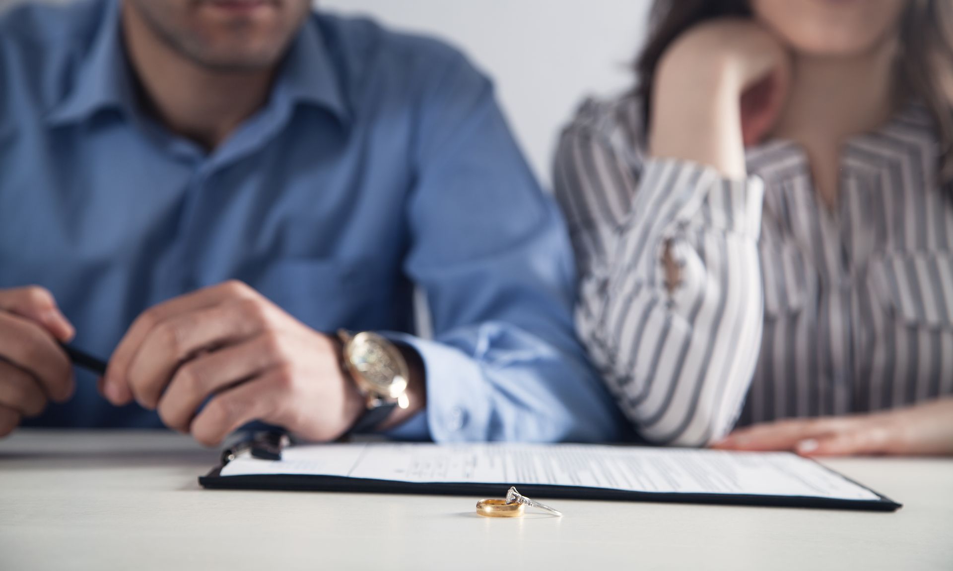 A couple sitting at a table with divorce paperwork and two wedding rings placed in front of them A couple sitting at a table with divorce paperwork and two wedding rings placed in front of them