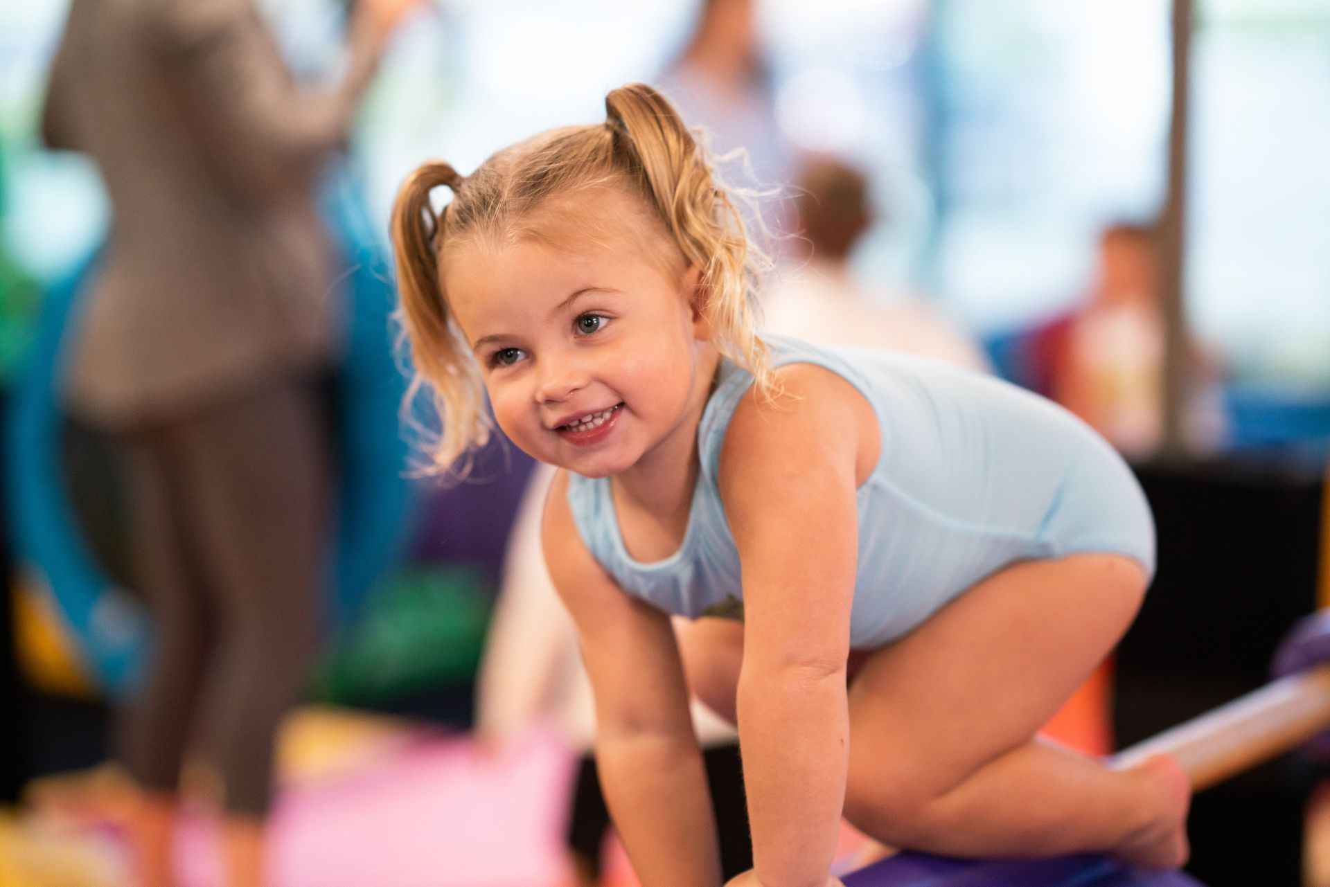 A little girl is crawling on a balance beam in a gym.