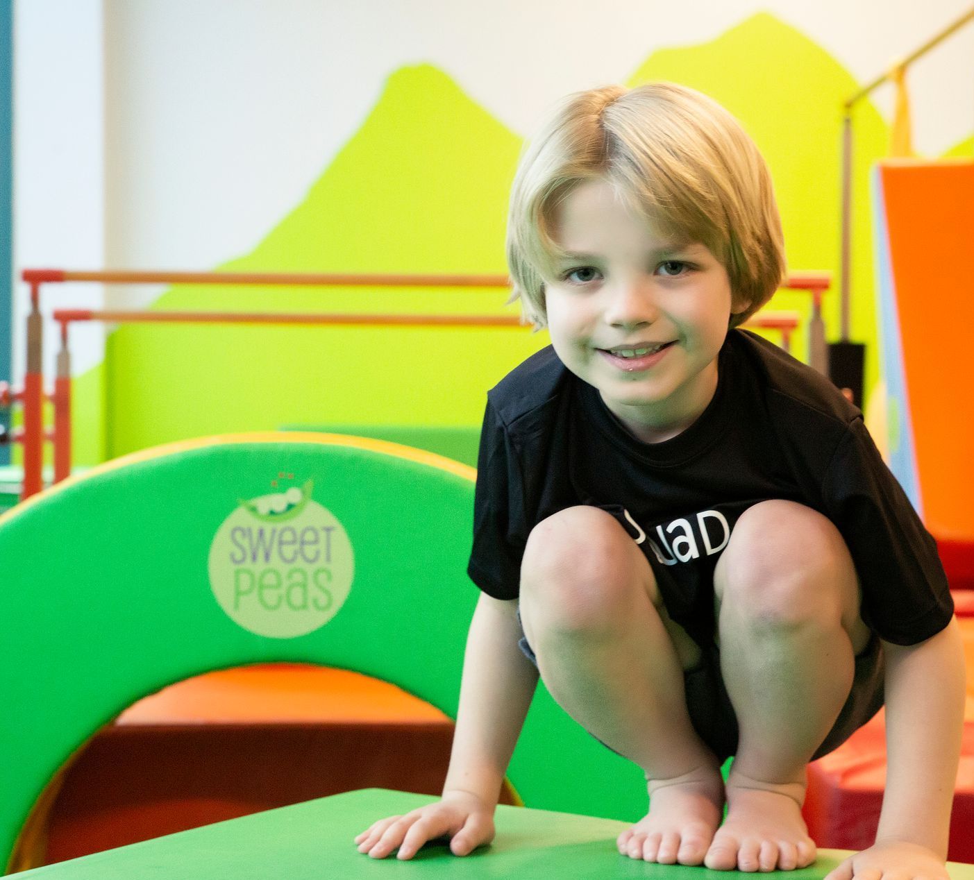 A young boy is squatting down in front of a sweet peas sign