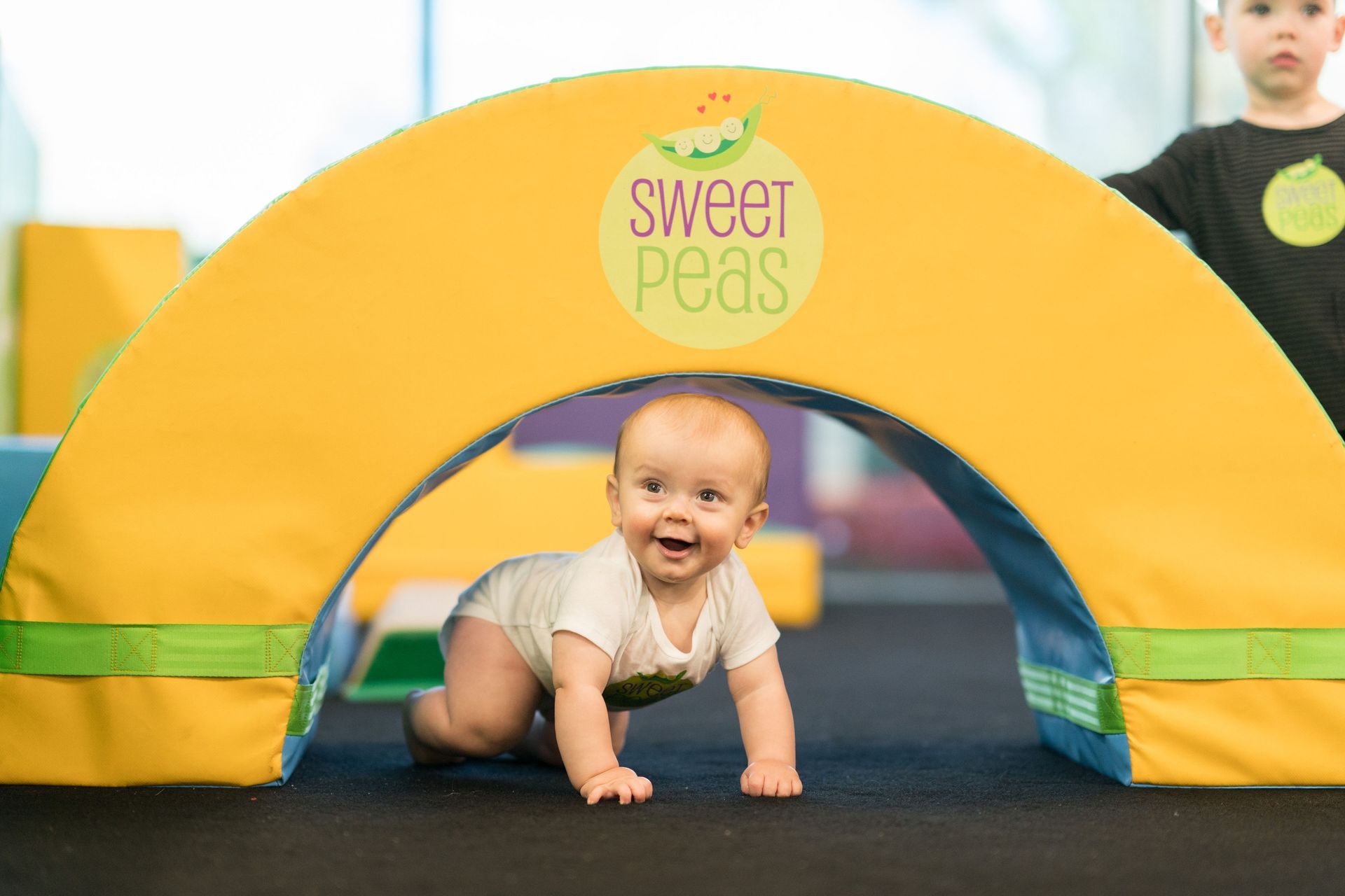 A baby is crawling through a yellow arch.