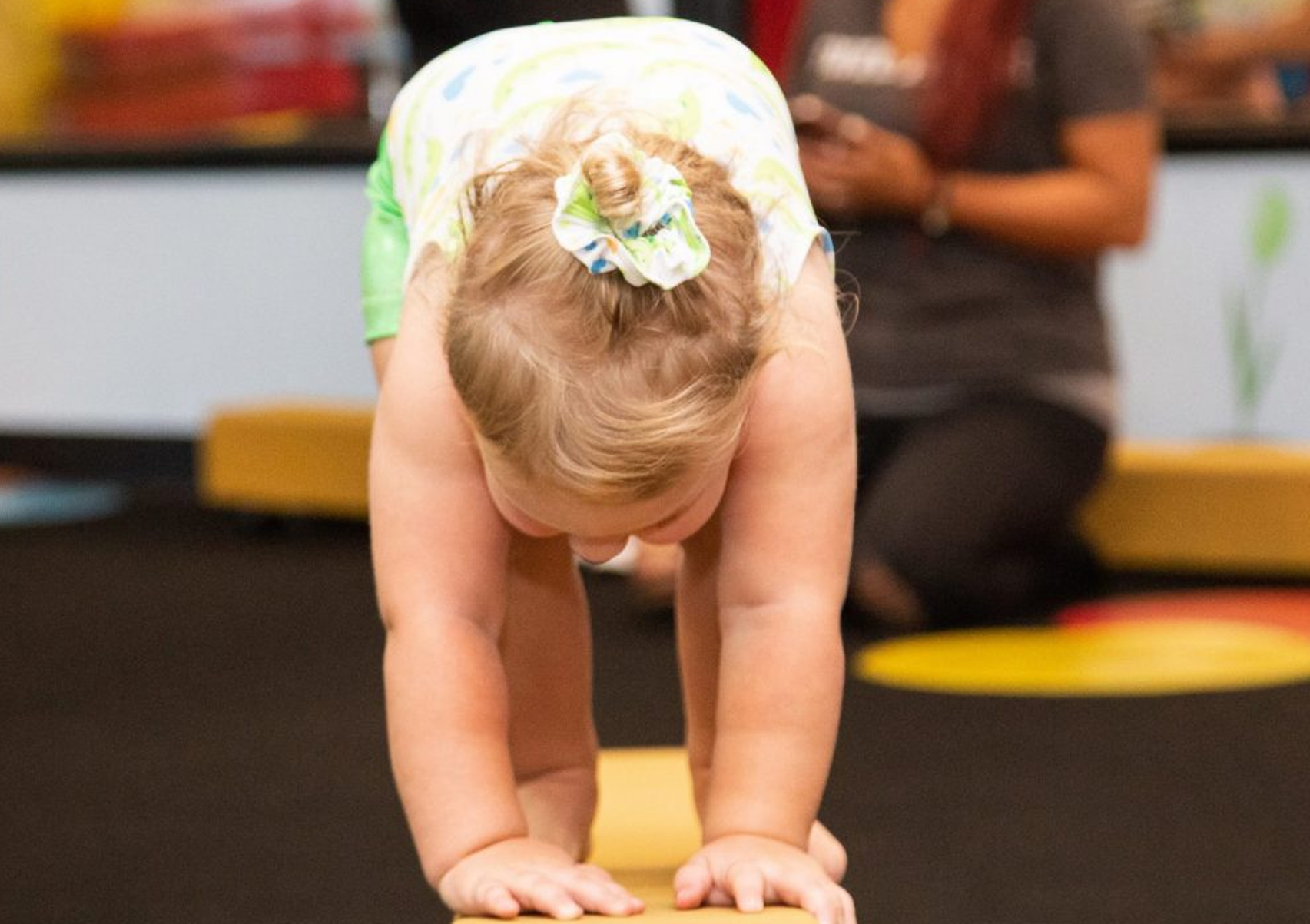 A baby girl is doing a handstand on a balance beam.