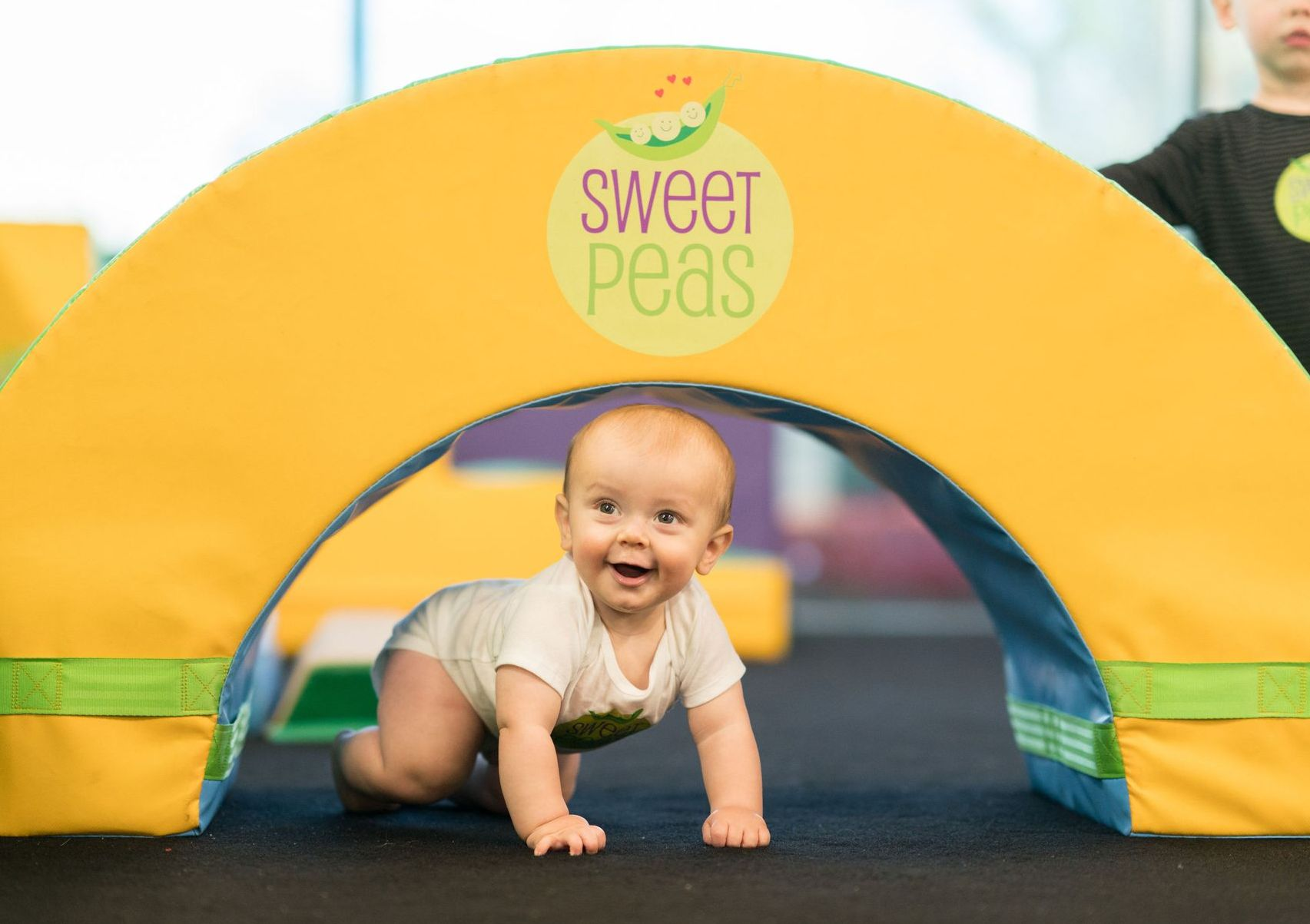 A baby is crawling through a yellow arch.
