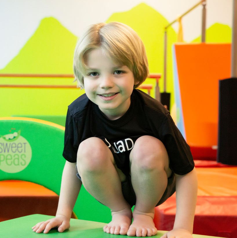 A young boy is squatting down in front of a sign that says sweet peas