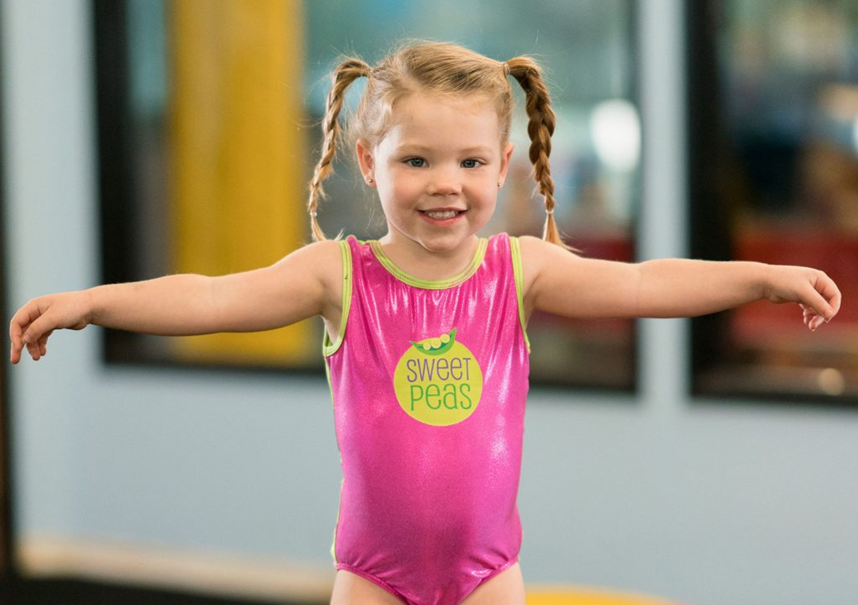 A little girl in a pink leotard is standing on a balance beam.