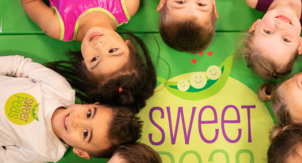 A group of children are laying on their backs on a green mat.