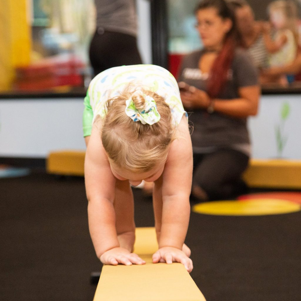 A baby girl is doing a handstand on a balance beam.