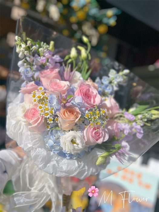 一束用透明塑料包裹的粉色、白色和淡紫色花朵,摆放在户外。