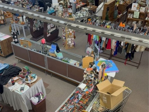 Indoor flea market with tables of assorted goods, clothing racks, and open cardboard boxes.